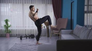 boxer homem fazendo sombra boxe de adicionando pontapé depois de socos às lar. jovem atleta homem fazendo sombra boxe às casa com velozes e poderoso socos, chutes. video