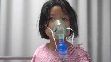 Little Asian girl having an oxygen mask and breathing through a nebulizer at the hospital. Concept of bronchitis, respiratory and Medical treatment. video