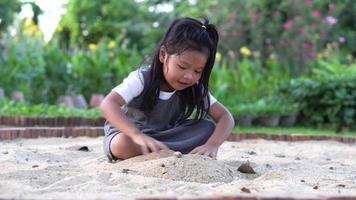 Little Asia girl sitting in the sandbox and playing whit toy shovel bucket and she was scooping in toy shovel bucket. Playing is a learning development and builds muscle for children. video