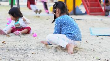 el pequeño asiático niña es jugando el arena en el patio de juegos. jugando es un aprendizaje desarrollo. y construir músculo para niños. video