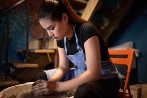 cerámica artista, joven hembra haciendo un pedazo de arcilla moldura tranquilamente y meticulosamente en orden a Produce el más atractivo trabajo posible, foto