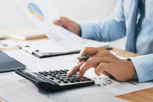 businessman use calculator and computer holding paper work with pen on desk in office. finance and accounting concept photo