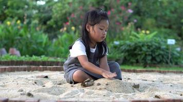 Little Asia girl sitting in the sandbox and playing whit toy shovel bucket and she was scooping in toy shovel bucket. Playing is a learning development and builds muscle for children. video