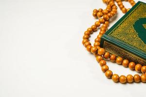 The Holy Al Quran with written arabic calligraphy meaning of Al Quran and rosary beads or tasbih on white background, isolated with copy space. photo