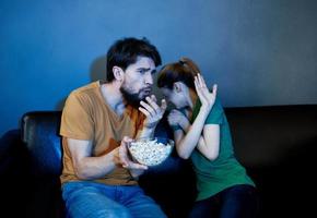 un hombre y un asustado mujer acecho un película en el noche en el sofá con un plato de palomitas de maíz foto