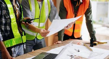 Contractor and architect looking at plan, tablet, laptop and talking about working on big project. Building in construction process interior. team work photo