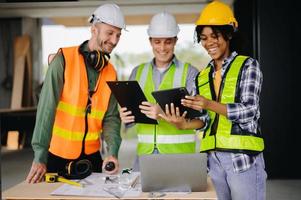 colleagues discussing data working and tablet, laptop with on on architectural project at construction site at desk in office photo