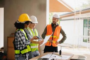 Contractor and architect looking at plan, tablet, laptop and talking about working on big project. Building in construction process interior. team work photo