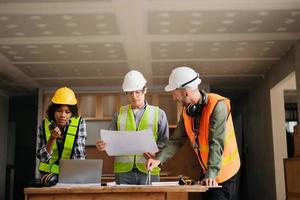 Contractor and architect looking at plan, tablet, laptop and talking about working on big project. Building in construction process interior. team work photo