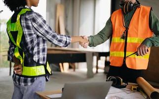 Construction team shake hands greeting start new project plan behind yellow helmet on desk in office center to consults about their building project. photo