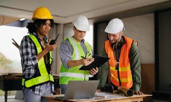 Contractor and architect looking at plan, tablet, laptop and talking about working on big project. Building in construction process interior. team work photo