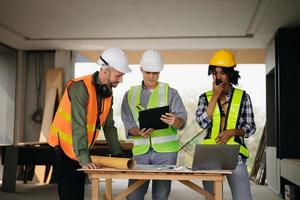 Contractor and architect looking at plan, tablet, laptop and talking about working on big project. Building in construction process interior. team work photo
