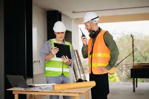 Contractor and architect looking at plan, tablet, laptop and talking about working on big project. Building in construction process interior. team work photo