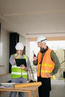 Contractor and architect looking at plan, tablet, laptop and talking about working on big project. Building in construction process interior. team work photo