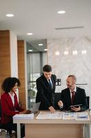 empresarios felices mientras colaboran en un nuevo proyecto en una oficina. grupo de diversos empresarios que usan una computadora portátil y una tableta en la oficina. foto