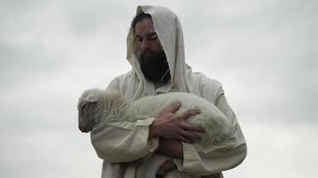 une aimant berger en portant une bébé mouton, agneau dans le sien bras video