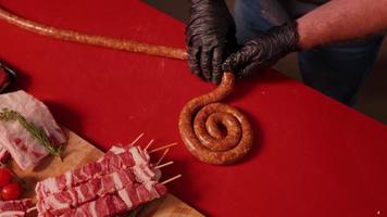Cook rolling a long homemade sausage ring on a red table in the kitchen. video