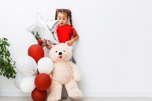 Happy brightful image of cute joyful little girl with balloons isolated on background. Amazing charming birthday fashionable kid looking to camera photo