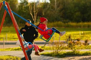 Happy little girlfriends on swing in park photo