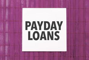 white sticker with text payday loans on pink wooden background photo