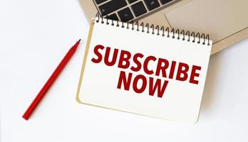 Laptop, red pen and notepad with text subscribe now in the white background photo