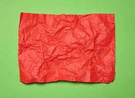 Crumpled rectangular sheet of red paper on a green background, top view. Place for inscription photo