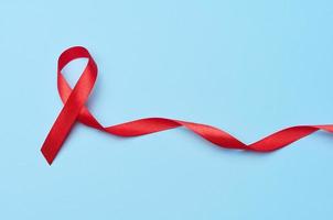 A silk red ribbon in the form of a bow is isolated on a blue background, a symbol of the fight against AIDS and a sign of solidarity and support photo