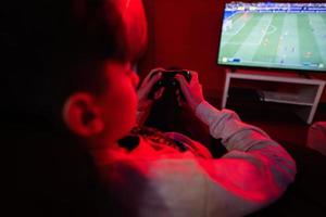 Teenager boy gamer play football gamepad video game console in red gaming room. photo
