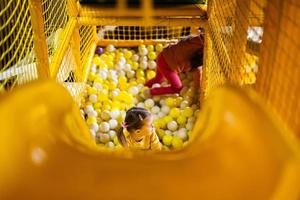 hermanos jugar con de colores pelotas a amarillo patio de recreo parque. hermanas en activo entretenimientos foto