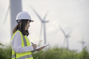 women engineer working and holding the report at wind turbine farm Power Generator Station on mountain,Thailand people photo