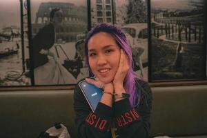 A woman with purple hair holding a phone photo