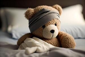 A sick teddy bear with a bandage on his head lies in bed with a fever and a headache. photo