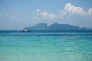 The yacht parking in the calm sea with moving paddle boat and mountain with blue sky in background photo