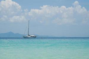 The yacht parking in the calm sea with moving paddle boat and mountain with blue sky in background photo