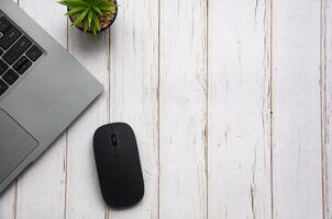 Top view of laptop, table plant and mouse on white wooden table with customizable space for text. Copy space photo