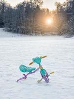 Abandoned broken children's bike in the snow. The end of the holidays. photo