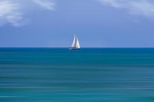 calm sea landscape with white sailboat against blue sky and long water time photo