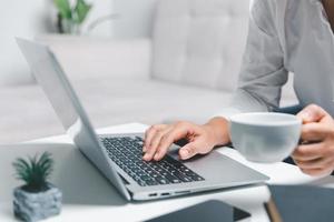 Social media day concept. Female freelancer starting working day early in morning drinking coffee in living room for website with using modern laptop computer. Businesswoman working in home office. photo