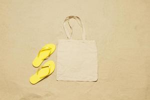 Mockup shopper handbag beach sand background. Top view copy space shopping eco reusable bag. Flip flops accessories. Template blank top view white cotton material canvas cloth. Empty mock-up beach photo