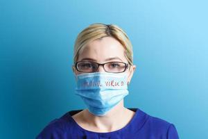 Portrait of pretty woman wearing medical mask with coronavirus text at blue background. Coronavirus concept. Respiratory protection. photo