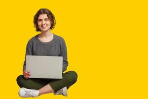 Pretty Indian asian young girl using laptop computer isolated over yellow background photo