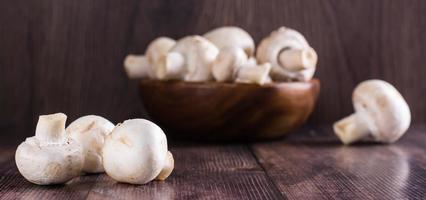 Close-up whole fresh champignons on a wooden table and in a bowl on the background web banner photo