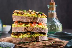 Close-up of a layered rye bread sandwich with guacamole, fried mushrooms, tomatoes and dill photo
