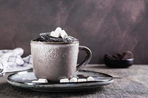 Chocolate cake in a mug with marshmallows and powdered sugar on the table for homemade dessert photo