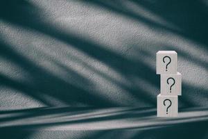 Wooden Cube with Question Mark Icons on Dark Concrete Table with Light Beam, and Shadow Background, Suitable in Business Concept. photo