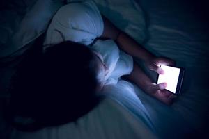 mujer asiática jugando en el teléfono inteligente en la cama por la noche, gente de Tailandia, adicto a las redes sociales foto