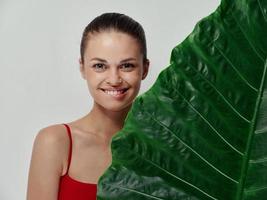 woman in a red t-shirt stands behind a leaf of a palm tree on a light background clean skin photo