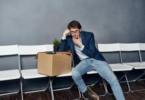 disgruntled man sitting on chairs with a box job search photo