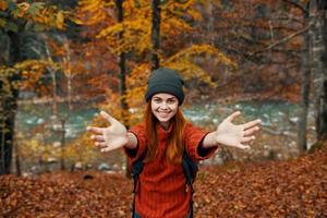 contento mujer caminante en el otoño bosque cerca el río gesticulando con su manos Copiar espacio foto