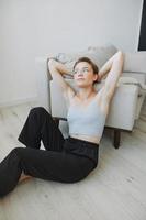 Teenage girl sitting on the floor at home smiling in home clothes and glasses with a short haircut, lifestyle without filters, free copy space photo